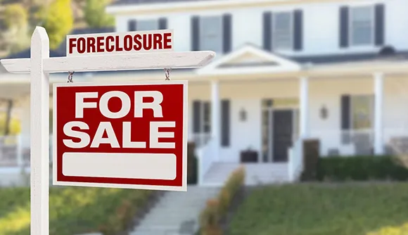 Foreclosure sign in front of a house with white columns, indicating a property for sale in Post Falls, ID.