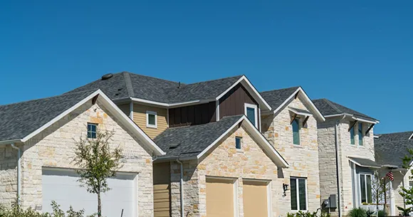Exterior of a two-story house with gray siding, white trim, and a double garage, under a clear blue sky.